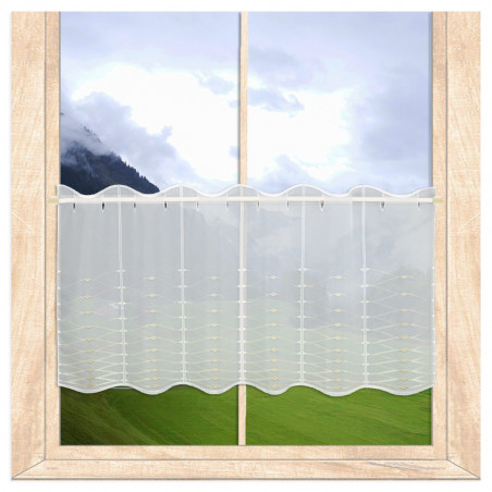 Halbtransparente Scheibengardine mit beiger Stickerei am Fenster vor Berglandschaft montiert.