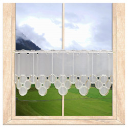Halbtransparente Scheibengardine mit beiger Stickerei am Holzfenster im gemütlichen Raumambiente.