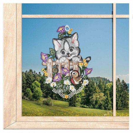 Gesticktes Fensterbild mit einer Katzen auf einem Holzzaun im idyllischen Frühlings-Ambiente am Fenster.