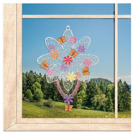 Plauener Spitze Fensterbild mit bunten Blüten am Fenster vor einer Frühlingswiese.