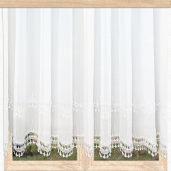 Halbtransparente weiße Gardine mit ornamentaler Stickerei und Bogensaum im hellen Landhausstil vor Fensterausblick.
