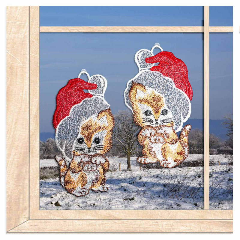 Filigrane Weihnachts-Fensterbilder aus Spitze mit Katzen-Motiv vor einem hellen Fenster mit winterlicher Kulisse.
