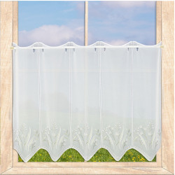 Weiße Landhaus-Gardine mit floralem Muster am Fenster vor Wiese, hochwertiger Sichtschutz aus Spitze.