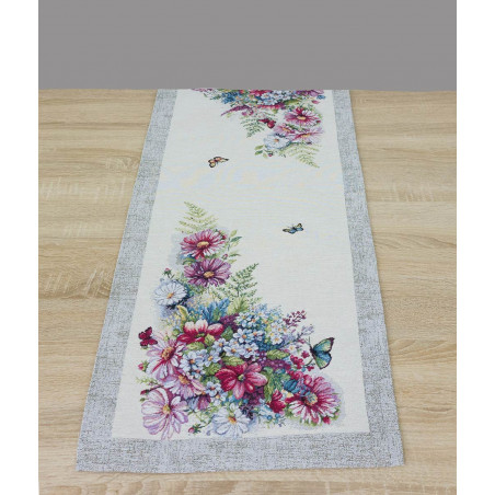 Der Tischläufer verfügt über einen cremefarbenen Grund mit einem markanten, grau melierten Randabschluss. Die Anordnung der Blumen sind in üppigen Eckmotiven zu sehen.