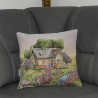 Ein kleines englisches Landhaus in einer üppig blühenden Landschaft mit einem Bach zeigt sich auf dieser verträumten Kissenhülle auf einem grauen Sofa.