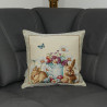 Auf einem grauen Sofa ist eine niedliches Osterkissen mit zwei Hasen und bunten Blumen in Gobelin-Webtechnick platziert.