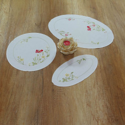 Weißes Tischwäsche-Set mit Mohnblumen-Stickerei und gelber Rosenkerze dekoriert auf hölzerner Tischplatte.