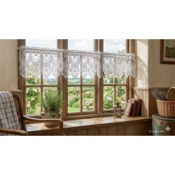 Die elegante weiße Spitzengardine Bella an einem sonnendurchflutetem Holzfenster.