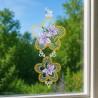 Gesticktes Fensterbild mit lila Orchideen in einem Medaillon vor hellem Natur-Ambiente am Fenster.