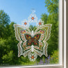 Filigranes Fensterbild mit buntem Schmetterling vor einem hellen Fenster mit Ausblick auf eine blühende Sommerwiese.