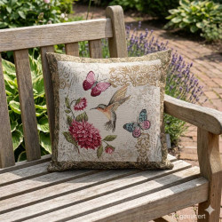 Exotisches Gobelin-Dekokissen mit Kolibri-Motiv auf einer eleganten Bank in einem hellen, stilvollen Garten.