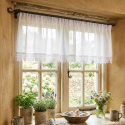 Weiße Bistro-Gardine aus Plauener Spitze am Küchenfenster mit Holzdeko, Kräutertöpfen und Frühlingsblumen.