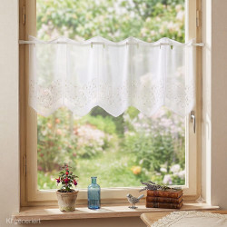 Weiße Kurzgardine aus Plauener Spitze mit Zick-Zack-Muster im Landhaus-Fenster mit Blick ins Grüne.