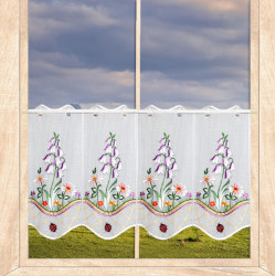 Kurzgardine in Weiß mit Glockenblumen-Stickerei und Marienkäfern als Heimtextilien im Fenster.
