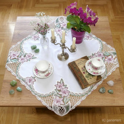 Elegante Tischdekoration mit bestickter Mitteldecke, Orchidee und Porzellantassen im Wohnzimmer.