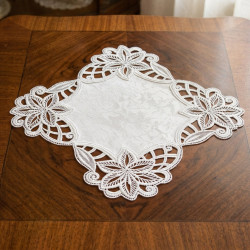 Quadratisches Spitzendeckchen in Reinweiß mit floralem Stickerei-Muster auf dunklem Holztisch platziert.