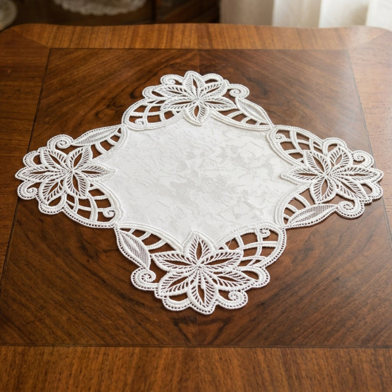 Quadratisches Spitzendeckchen in Reinweiß mit floralem Stickerei-Muster auf dunklem Holztisch platziert.