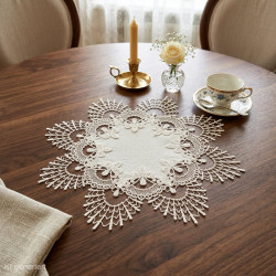 Rundes Spitze-Deckchen in Creme auf dunklem Holz-Esstisch dekoriert mit Kaffeetasse, Blumen und Kerze.