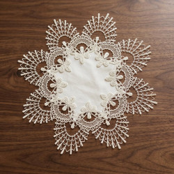Runder Spitzen-Tischset in Creme mit fächerartiger Bordüre flach auf dunklem Holzmöbel präsentiert.