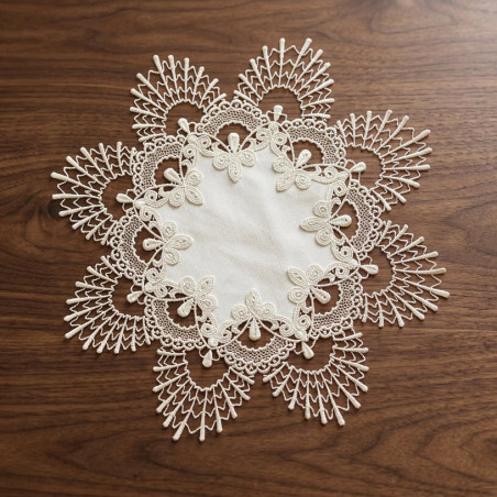 Runder Spitzen-Tischset in Creme mit fächerartiger Bordüre flach auf dunklem Holzmöbel präsentiert.